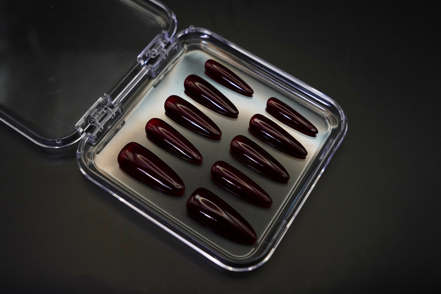 Vinklet bilde av Cherry on Top løsnegler i sitt åpne etui. De mandelformede neglene vises med sin dype, kirsebærrøde jelly-gloss finish.