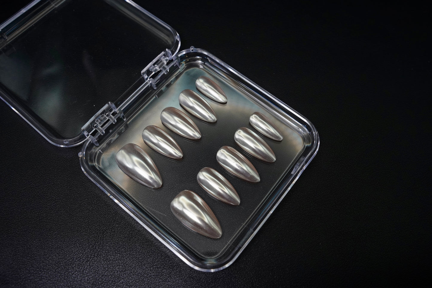Et komplett Silent Champagne negle sett vist fra siden. De mandelformede løsneglene har en subtil Chrome hvit-farge med en metallisk sateng-glans.