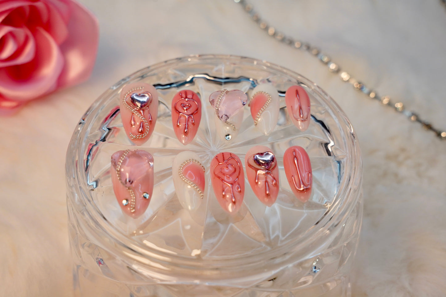 Stylet bilde av Pretty in Pain press on negler. Det romantiske og edgy neglesettet er presentert på et krystallglass med en rosa rose i bakgrunnen.