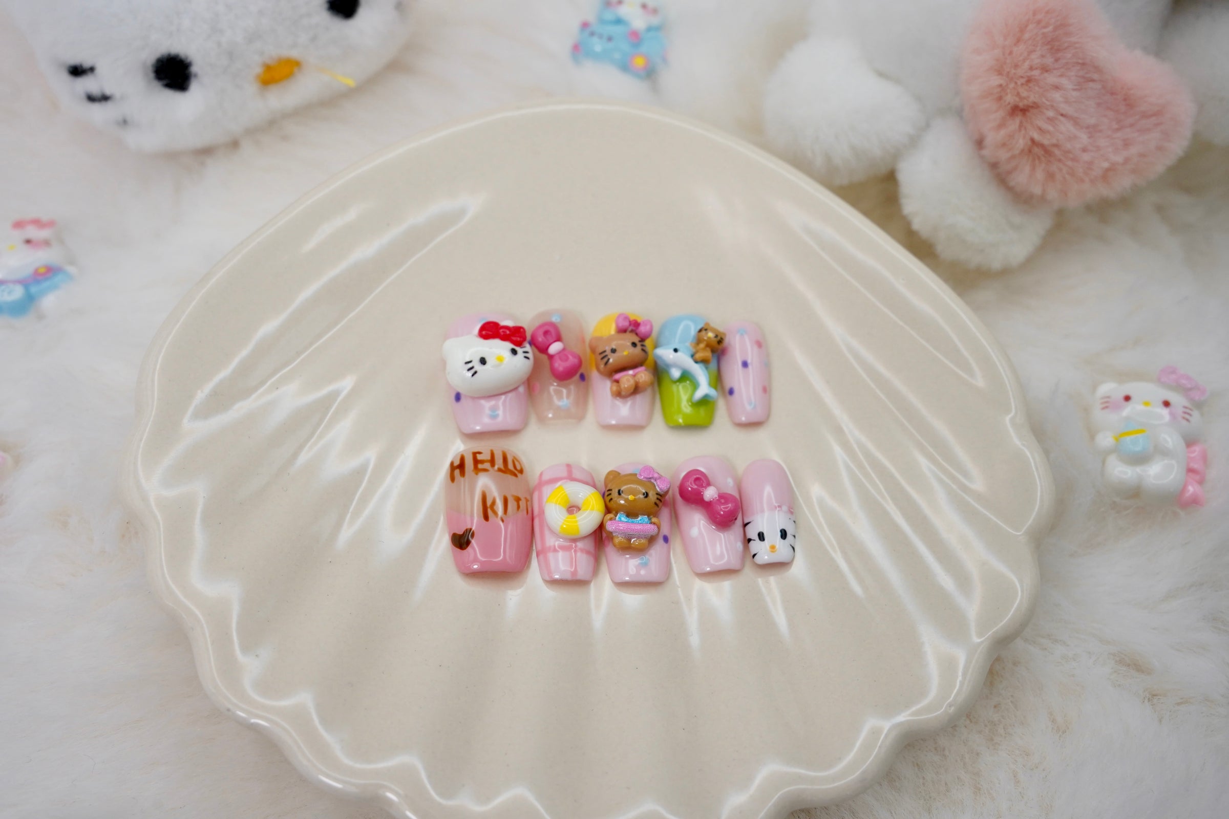Stylet bilde av Kitty Island press on negler for en full 'kawaii dream'-look. Neglesettet er presentert på et hvitt skjell-fat, omgitt av små Hello Kitty-figurer.
