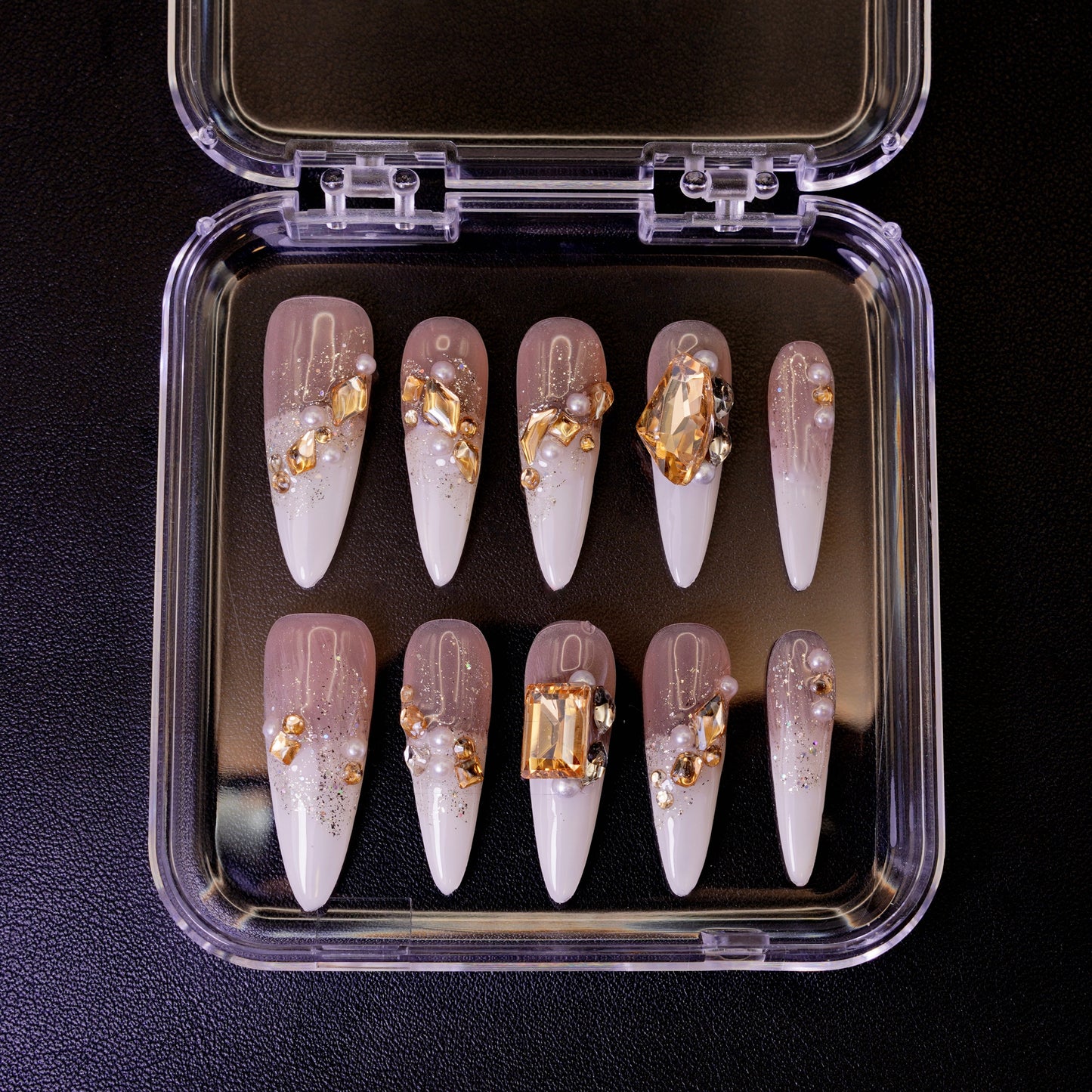 Ovenfra-bilde av Gold Digger's Gala press on negler i etui. Viser de lange stiletto-neglene med store, gullfargede edelstener og perler.