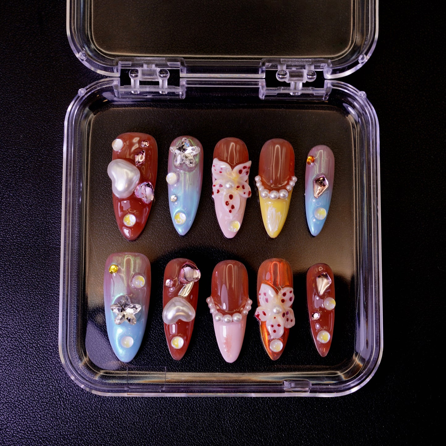 Ovenfra-bilde av det tropiske Starstruck in Waikiki press on negler-settet i etui. Viser de fargerike stiletto-neglene med 3D-blomster, perler og hjerte-charms.