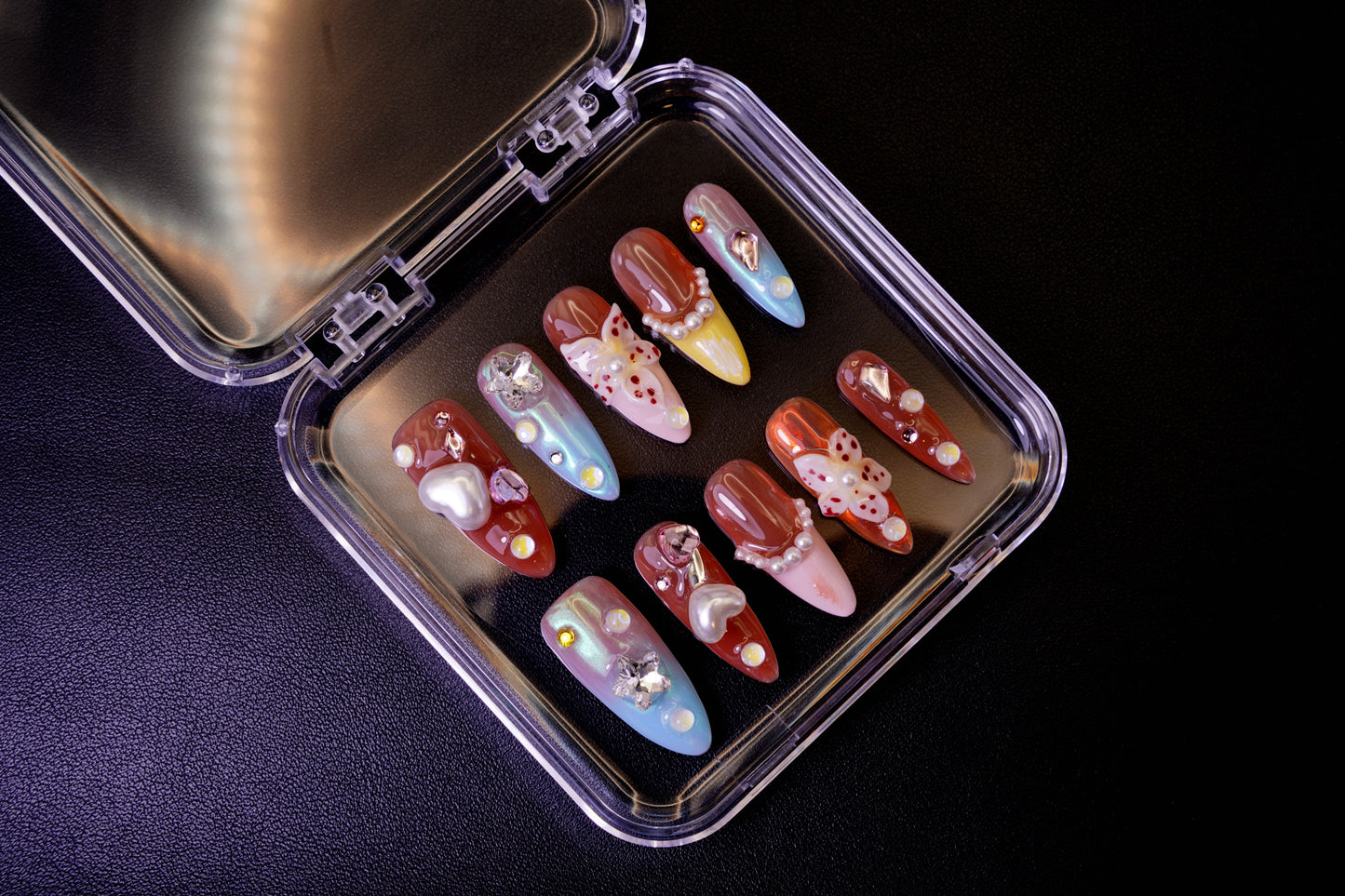 Et komplett Starstruck in Waikiki negle sett med et tropisk tema, vist i sitt åpne etui. Viser de ulike designene, inkludert en 3D-blomst, krom-hjerter og en livlig fargepalett.