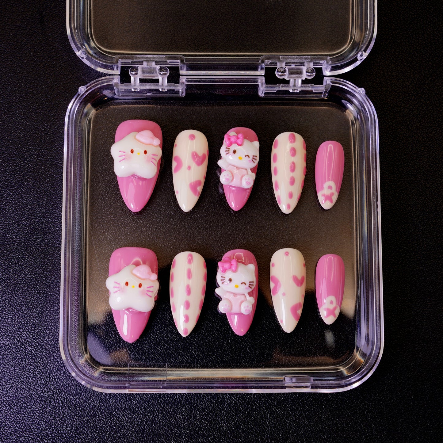 Ovenfra-bilde av Kawaii Crisis press on negler i etui. Viser de mandelformede neglene med 3D Hello Kitty-charms og rosa hjerter.