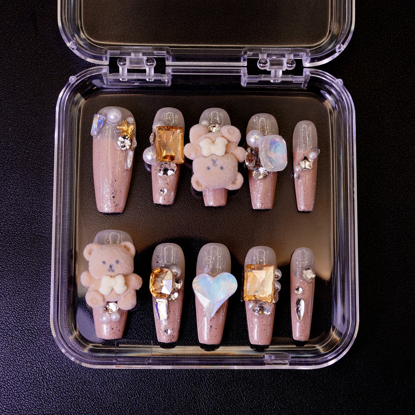 Ovenfra-bilde av Teddy Issues press on negler i etui. Viser de ballerina-formede neglene med 3D bamse-charms og store edelstener på en nude glitter-base.