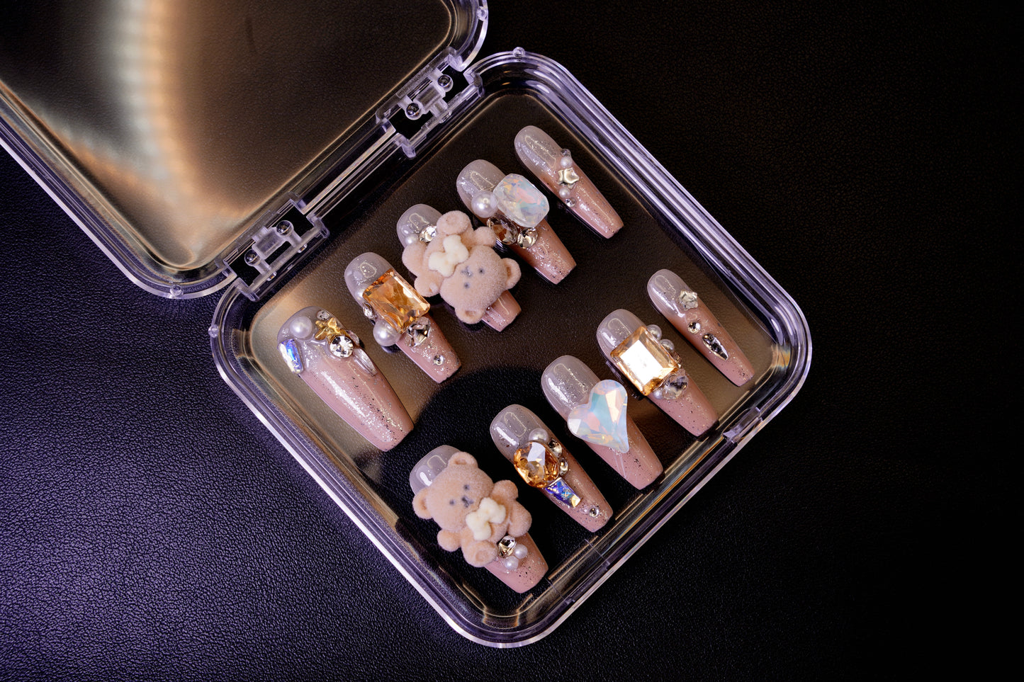 Et komplett, maksimalistisk Teddy Issues negle sett i sitt åpne etui. Viser de mange 3D-charmsene, inkludert bamser, hjerter og edelstener.