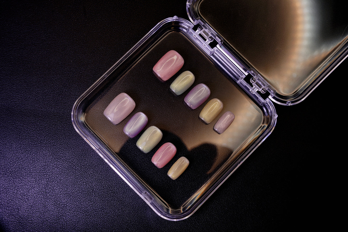 Vinklet bilde av Cotton Candy løsnegler. Viser den skinnende cat-eye-effekten på de pastellfargede, firkantede neglene.