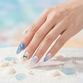 Hand with See me Glow press on nails on a sandy background with shells