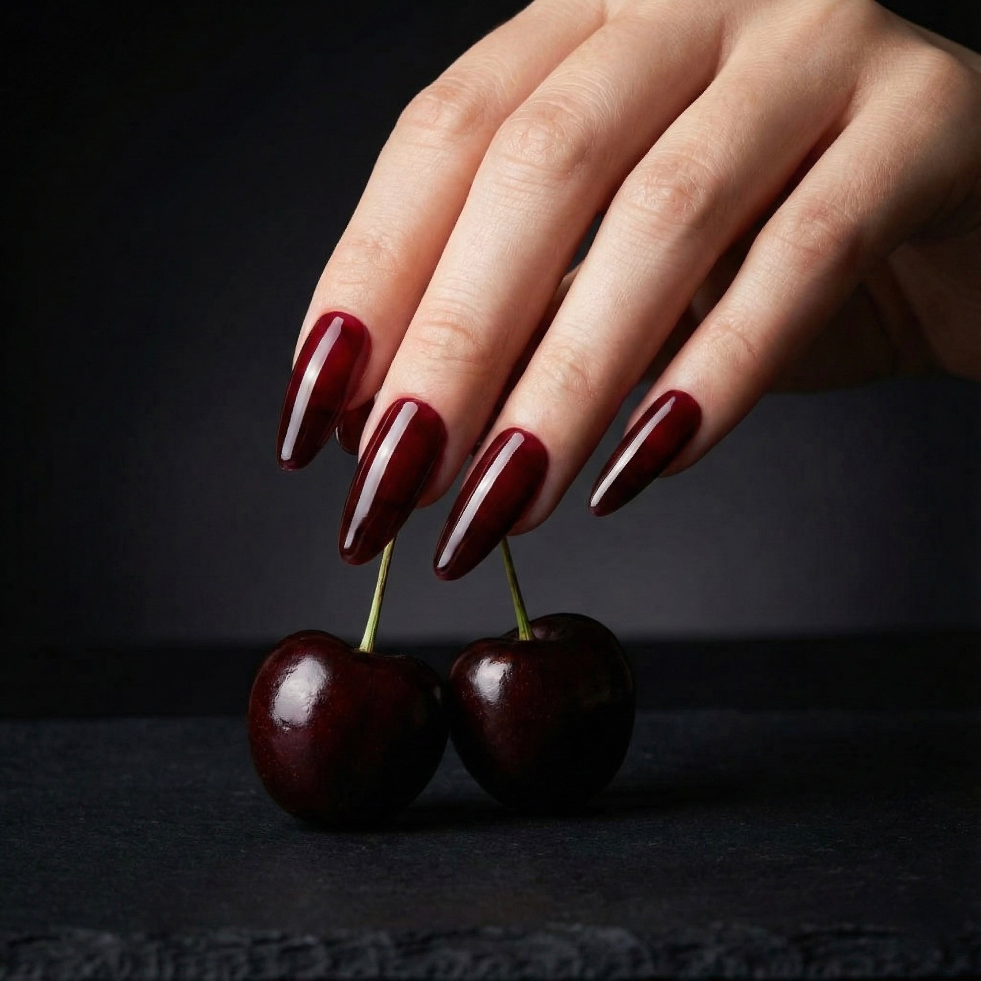Hand with Cherry on top press on nails polish holding two cherries against a black background
