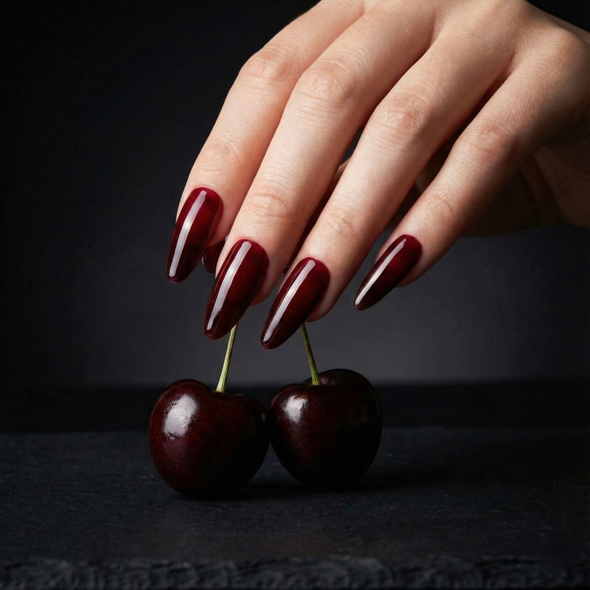 Hand with Cherry on top press on nails polish holding two cherries against a black background
