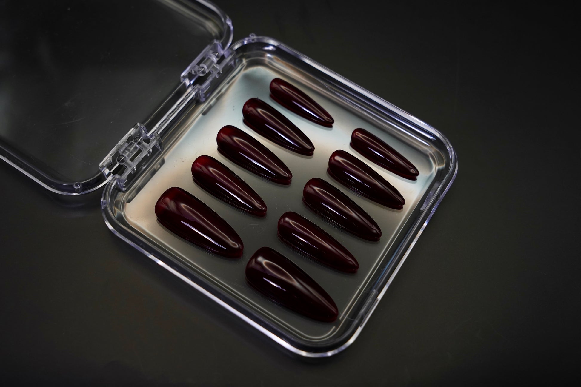 Vinklet bilde av Cherry on Top løsnegler i sitt åpne etui. De mandelformede neglene vises med sin dype, kirsebærrøde jelly-gloss finish.