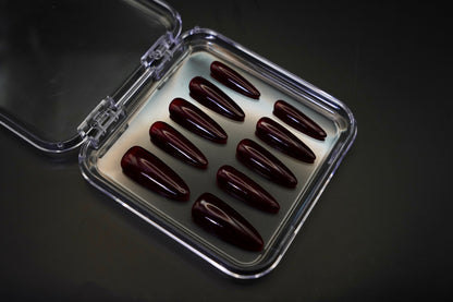 Vinklet bilde av Cherry on Top løsnegler i sitt åpne etui. De mandelformede neglene vises med sin dype, kirsebærrøde jelly-gloss finish.