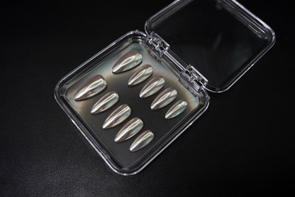 Vinklet bilde av Silent Champagne løsnegler. De mandelformede neglene med en luksuriøs satin-finish er vist i sitt åpne etui på en mørk bakgrunn.