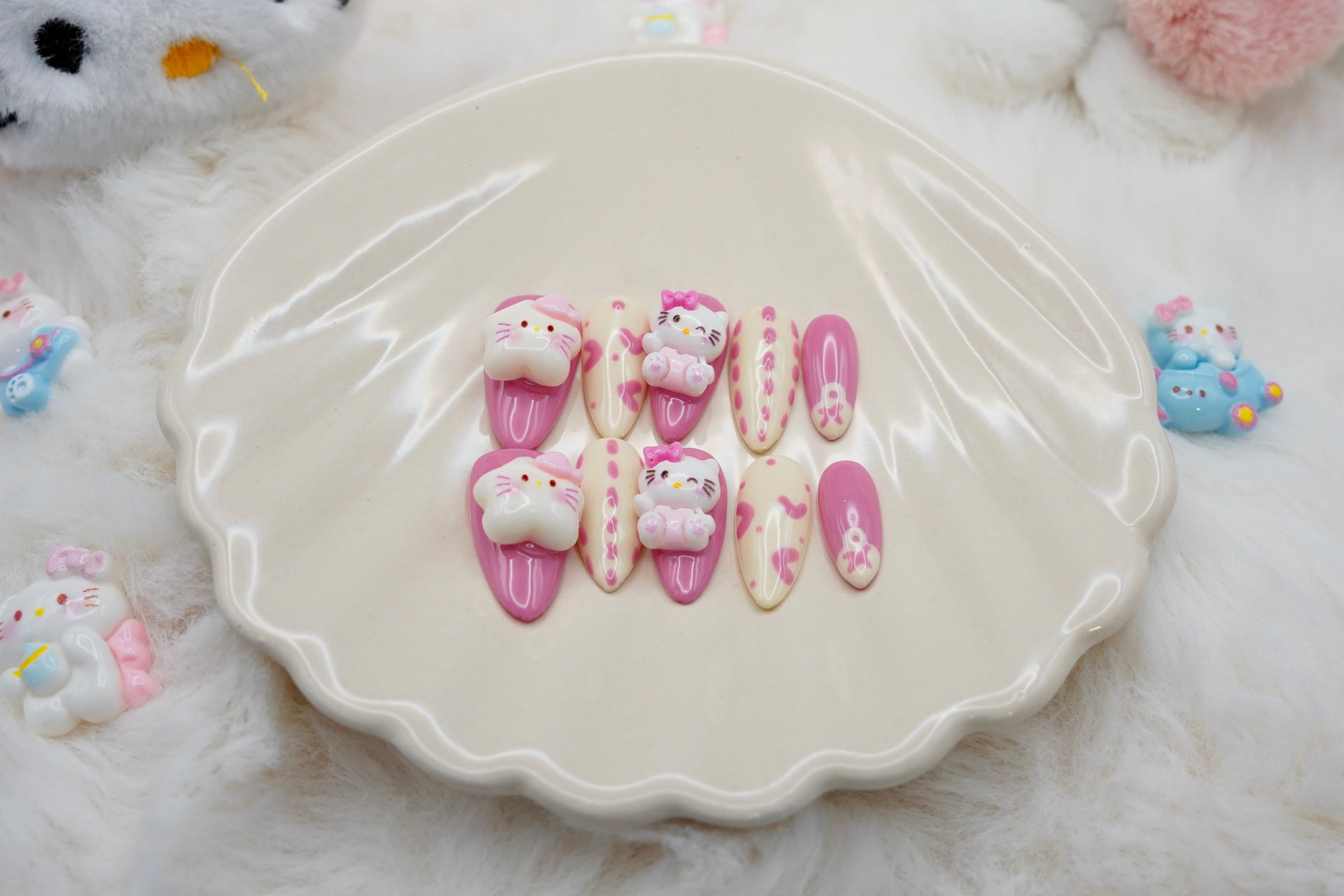 Stylet bilde av Kawaii Crisis press on negler for den ultimate kawaii-looken. Neglesettet er presentert på et hvitt skjell-fat og omgitt av små Hello Kitty-figurer.