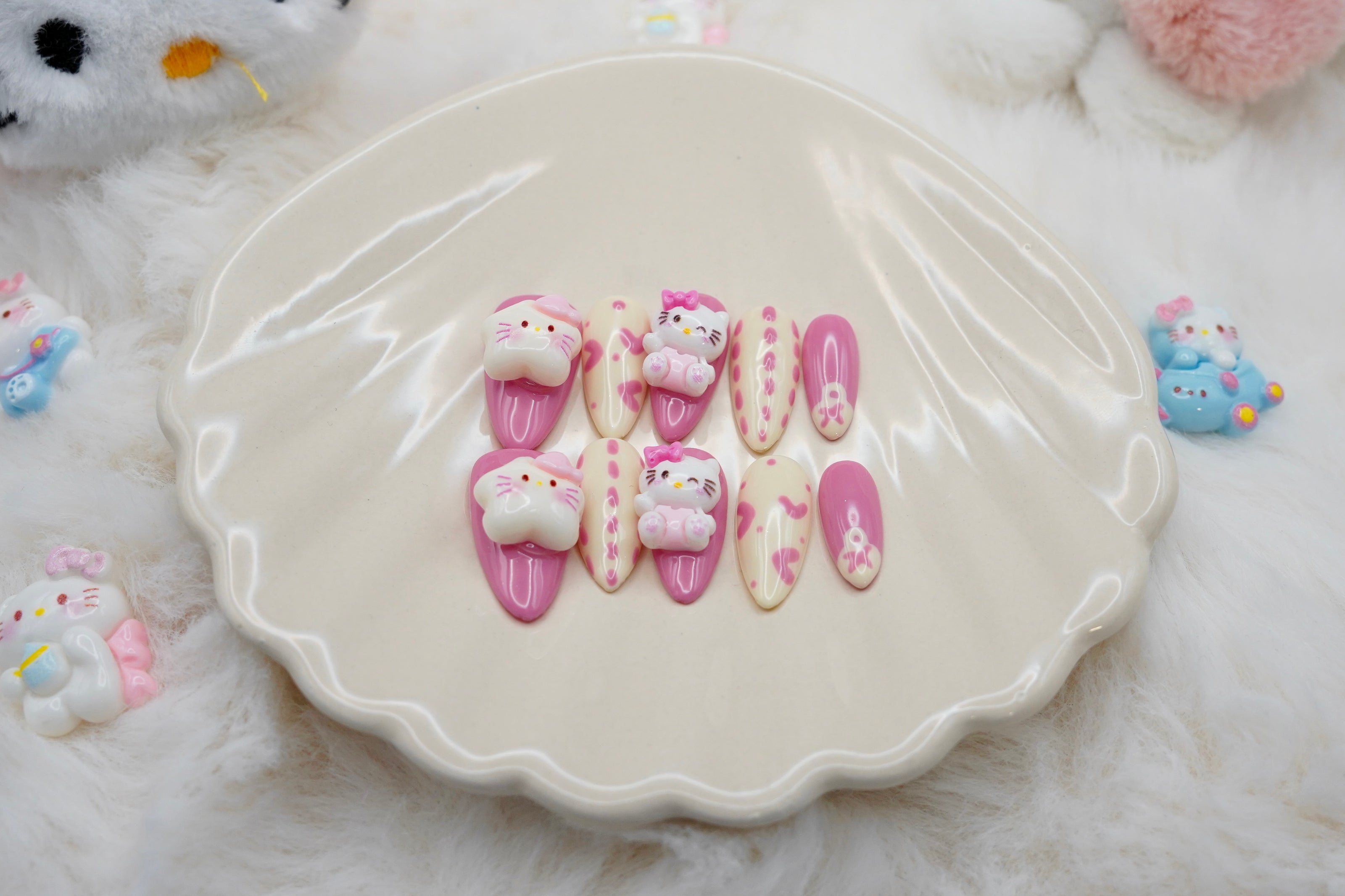 Stylet bilde av Kawaii Crisis press on negler for den ultimate kawaii-looken. Neglesettet er presentert på et hvitt skjell-fat og omgitt av små Hello Kitty-figurer.