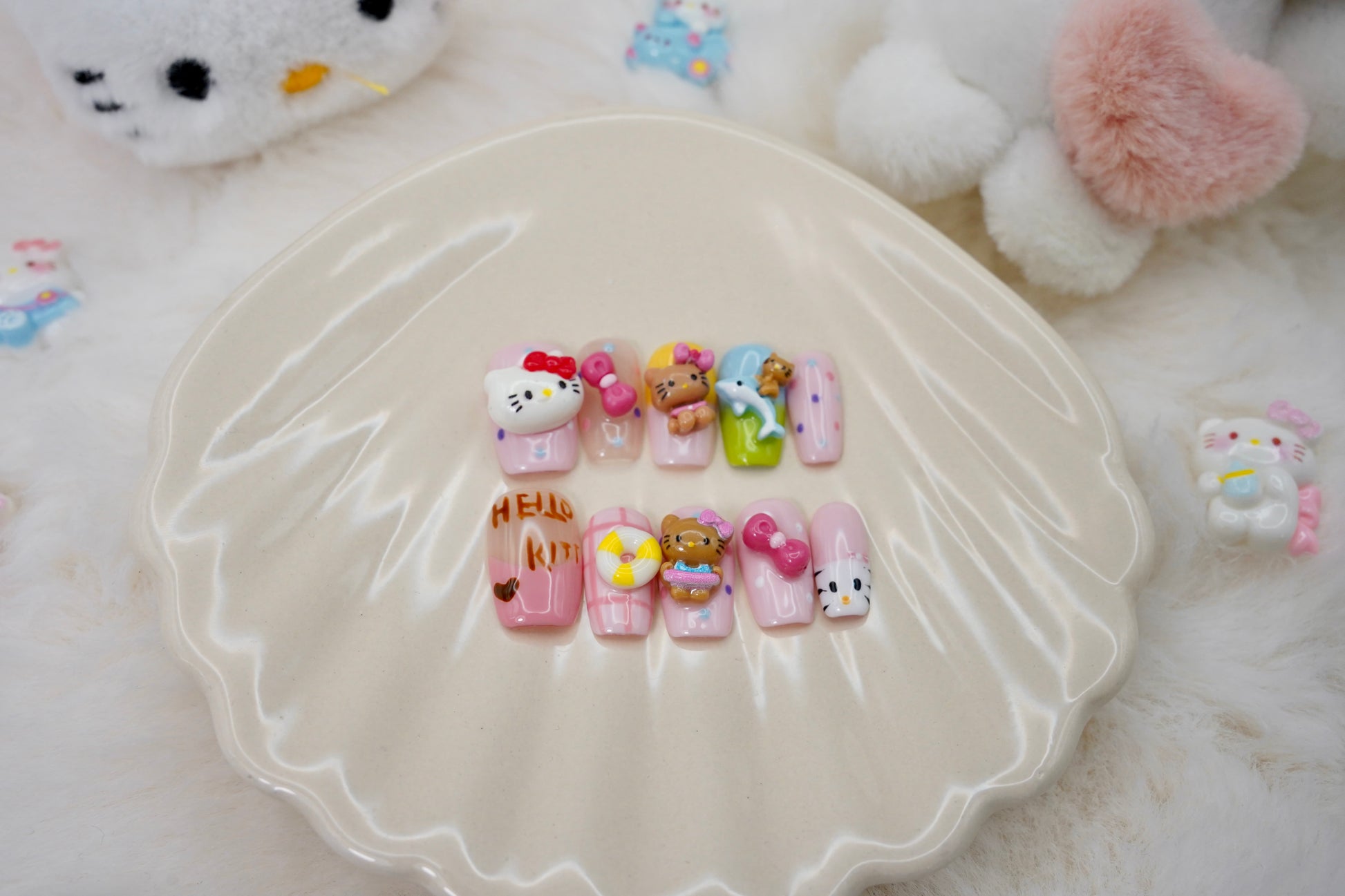 Stylet bilde av Kitty Island press on negler for en full 'kawaii dream'-look. Neglesettet er presentert på et hvitt skjell-fat, omgitt av små Hello Kitty-figurer.