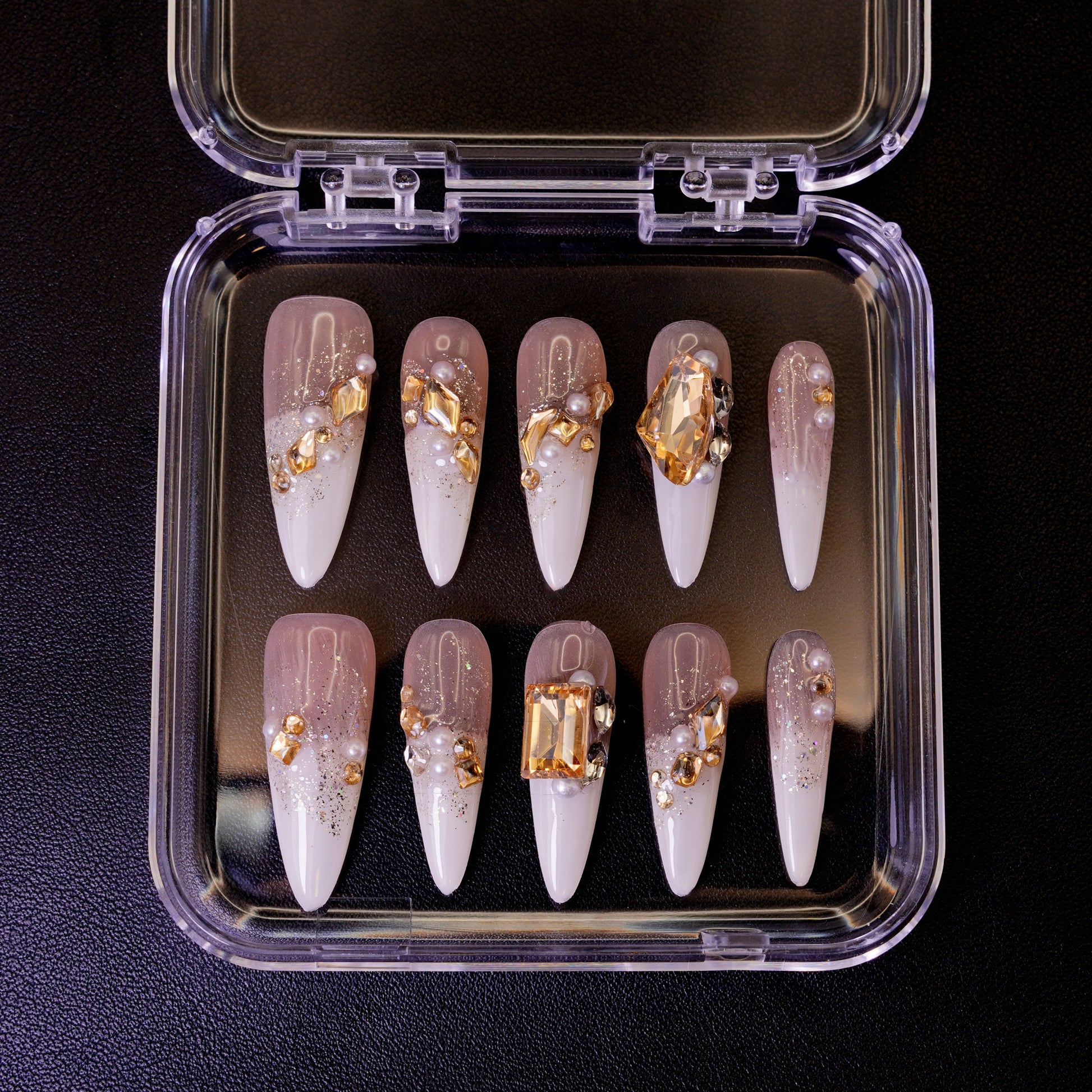 Ovenfra-bilde av Gold Digger's Gala press on negler i etui. Viser de lange stiletto-neglene med store, gullfargede edelstener og perler.