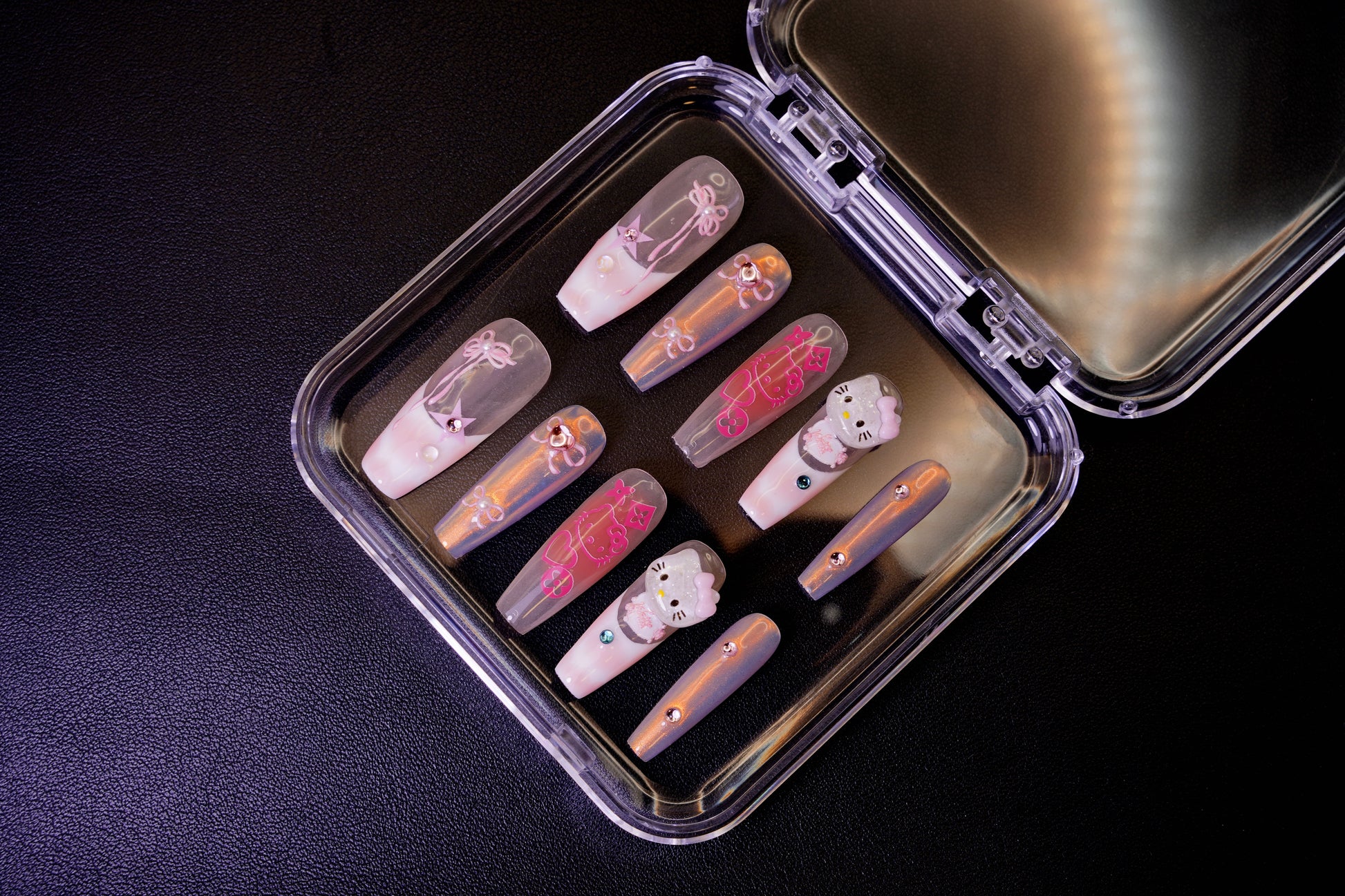 The Y2K Royalty nail set displayed from the side in its packaging. The holographic pink and chrome nails are shown with their 3D Hello Kitty and rhinestone details.