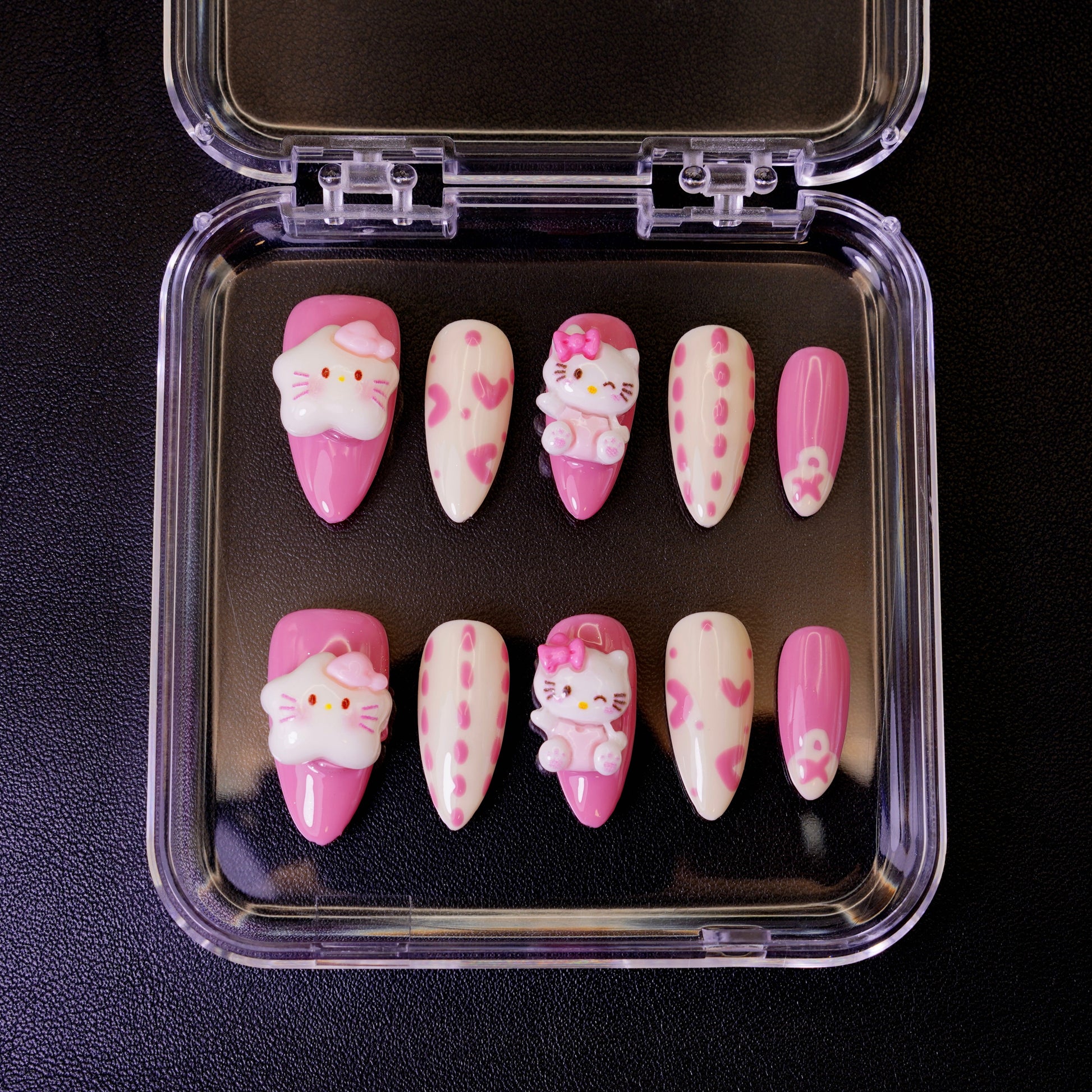 Ovenfra-bilde av Kawaii Crisis press on negler i etui. Viser de mandelformede neglene med 3D Hello Kitty-charms og rosa hjerter.