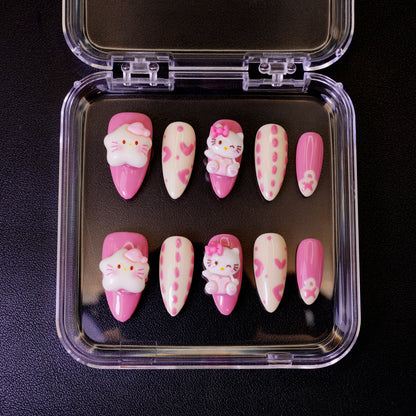 Ovenfra-bilde av Kawaii Crisis press on negler i etui. Viser de mandelformede neglene med 3D Hello Kitty-charms og rosa hjerter.