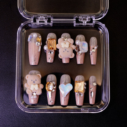 Ovenfra-bilde av Teddy Issues press on negler i etui. Viser de ballerina-formede neglene med 3D bamse-charms og store edelstener på en nude glitter-base.