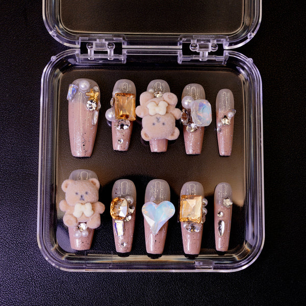 Ovenfra-bilde av Teddy Issues press on negler i etui. Viser de ballerina-formede neglene med 3D bamse-charms og store edelstener på en nude glitter-base.