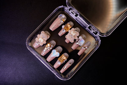 Vinklet bilde av Teddy Issues løsnegler som viser 3D-utsmykningene. De nude glitterneglene har myke bamse-charms og store, fasetterte edelstener.