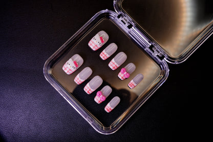 Vinklet bilde av Gingham Kitty løsnegler. De firkantede neglene vises med håndmalte, rosa gingham French tips og 3D-charms.