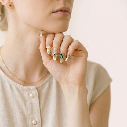 Styled Born Rich negler — gull-French almond-negler med smaragd mot mørkt stoff.