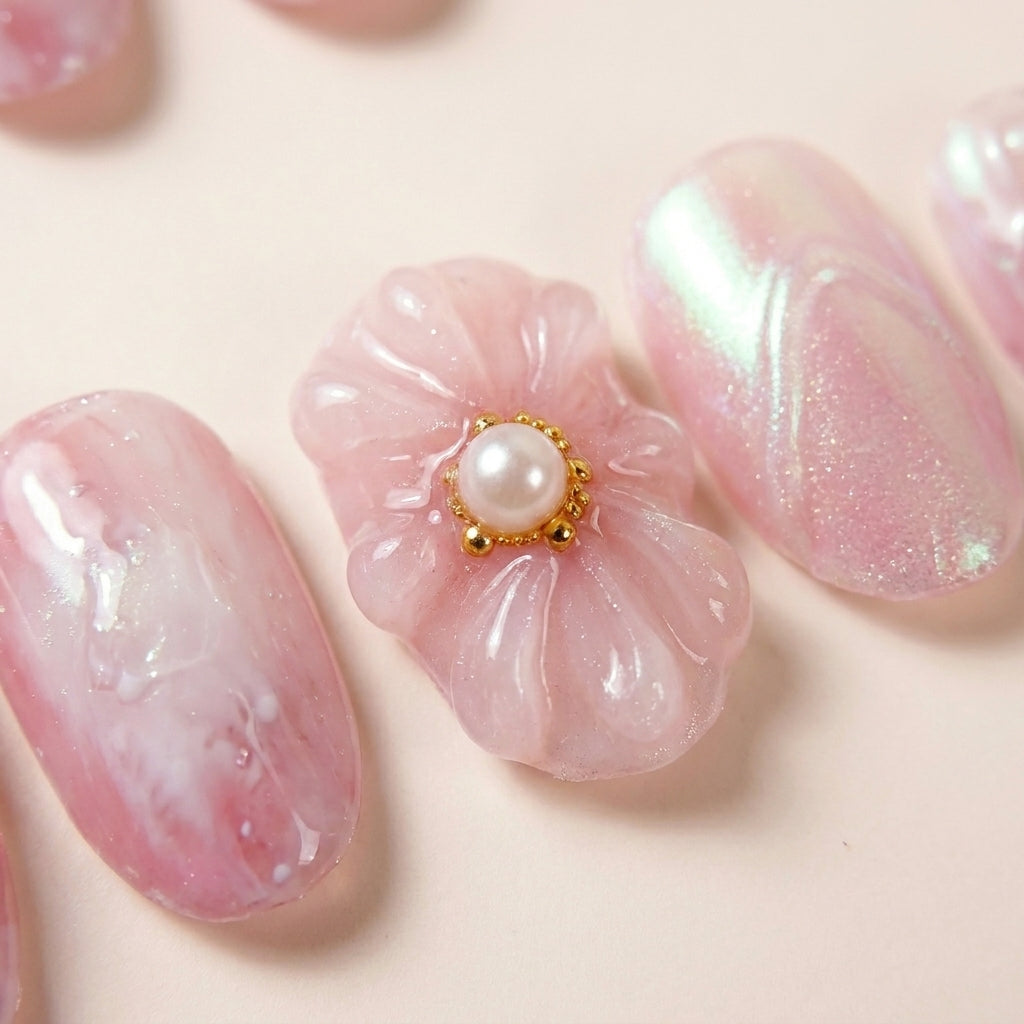 Makro-nærbilde av Flower Therapy løsnegler — falske negler med lim, med detaljer av 3D blomster-charm med gull og perle-sentrum, marmorert rosa base og chrome-relieff.