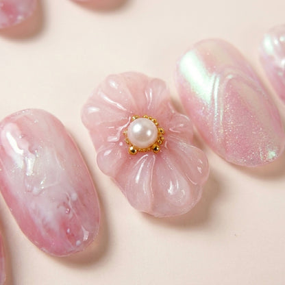 Makro-nærbilde av Flower Therapy løsnegler — falske negler med lim, med detaljer av 3D blomster-charm med gull og perle-sentrum, marmorert rosa base og chrome-relieff.
