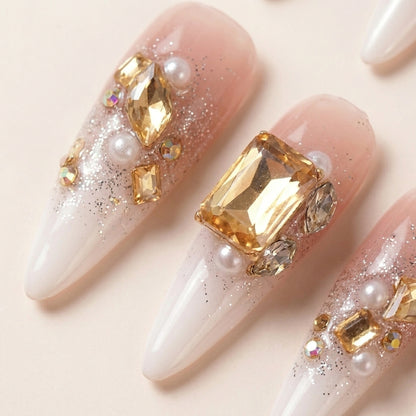 Makro-nærbilde av Gold Digger's Gala løsnegler — falske negler med lim, med detaljer av oversize gule og hvite edelstener, perler og sølvglitter på champagne ombré.