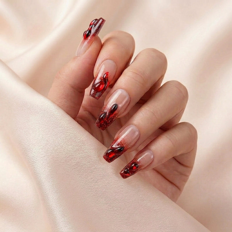 Hånd på lyserosa silkestoff med Hotter Than Revenge press on negler — håndlaget, gjenbrukbare coffin-negler med blodrød glitter-ombré og 3D drip-detaljer i hjerteform.