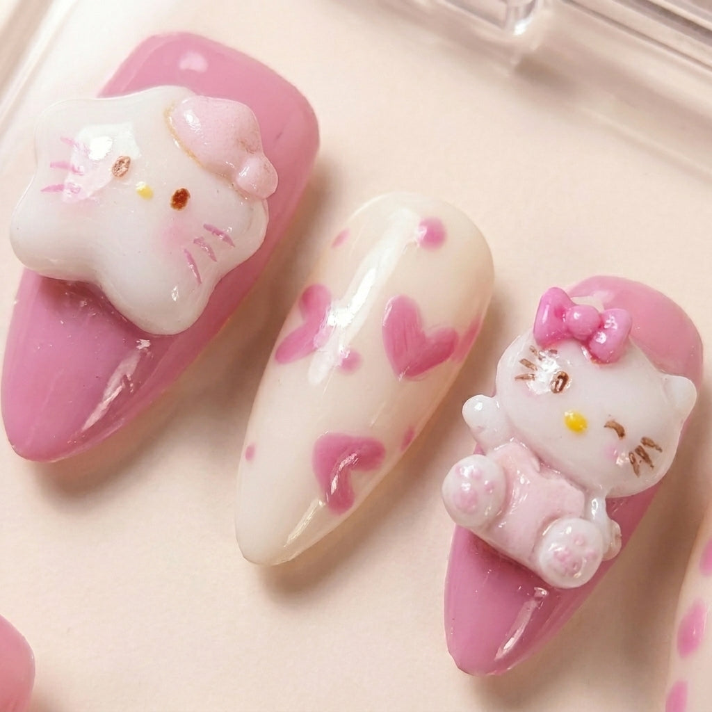 Makro-nærbilde av Kawaii Crisis løsnegler — falske negler med lim, med håndmalte rosa hjerter, almond-form og 3D Hello Kitty charms med stjerne-hatt.