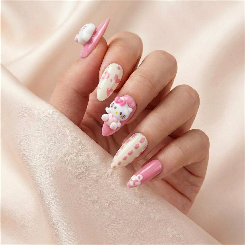 Hånd på lyserosa silkestoff med Kawaii Crisis press on negler — håndlaget, gjenbrukbare lange almond-negler med rosa hjerter, polka-dots og Hello Kitty charm med rosa sløyfe.