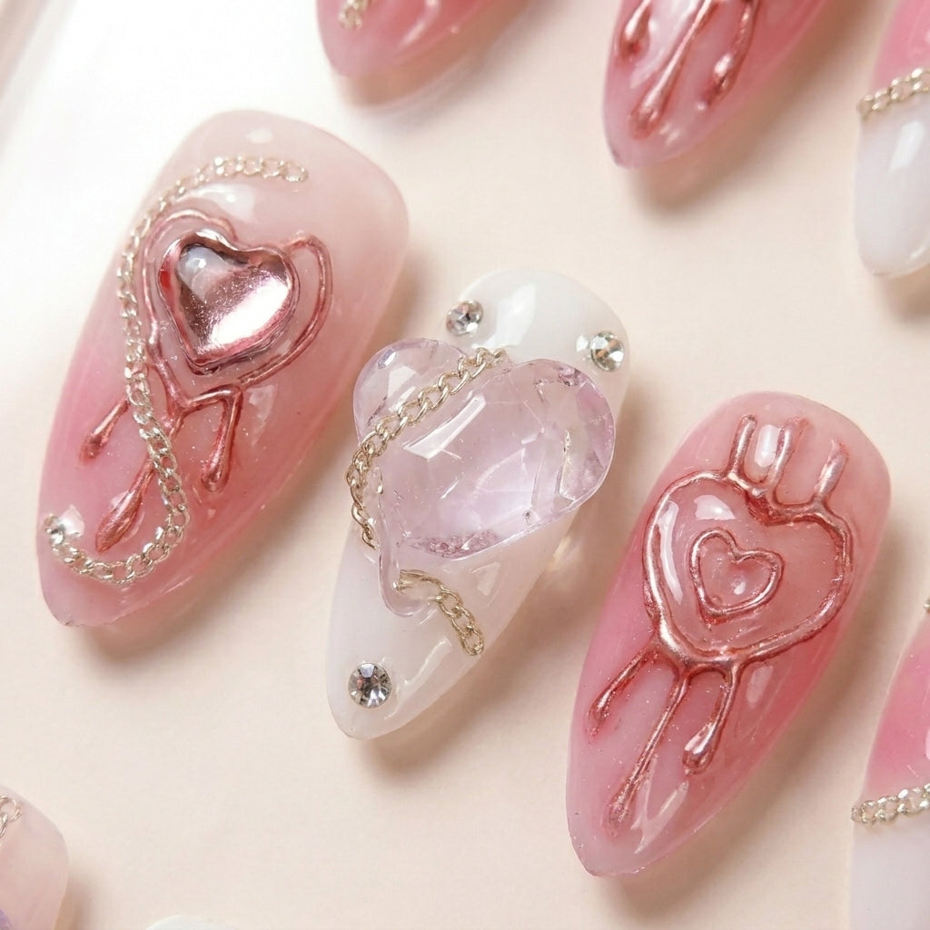 Makro-nærbilde av Pretty in Pain løsnegler — falske negler med lim, med detaljer av metallic rose-gold 3D hjerter, krystall hjerte-charm, sølvkjede og rhinestones.