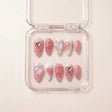 Pretty in Pain press on nails i etui — håndlaget lange almond-negler med rosa base, metallic rose-gold hjerte-drips, krystall hjerte-charms og sølvkjede-detaljer.