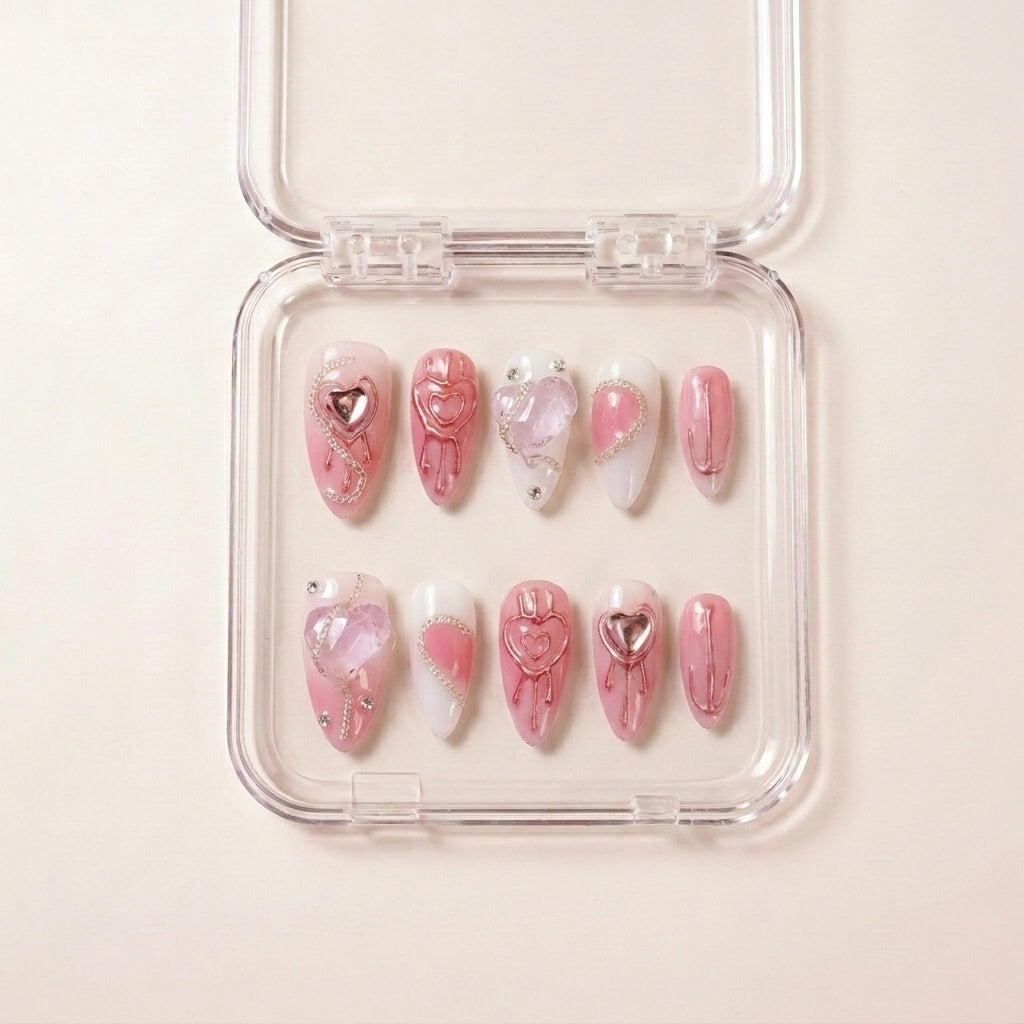 Pretty in Pain press on nails i etui — håndlaget lange almond-negler med rosa base, metallic rose-gold hjerte-drips, krystall hjerte-charms og sølvkjede-detaljer.