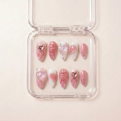 Pretty in Pain press on nails i etui — håndlaget lange almond-negler med rosa base, metallic rose-gold hjerte-drips, krystall hjerte-charms og sølvkjede-detaljer.
