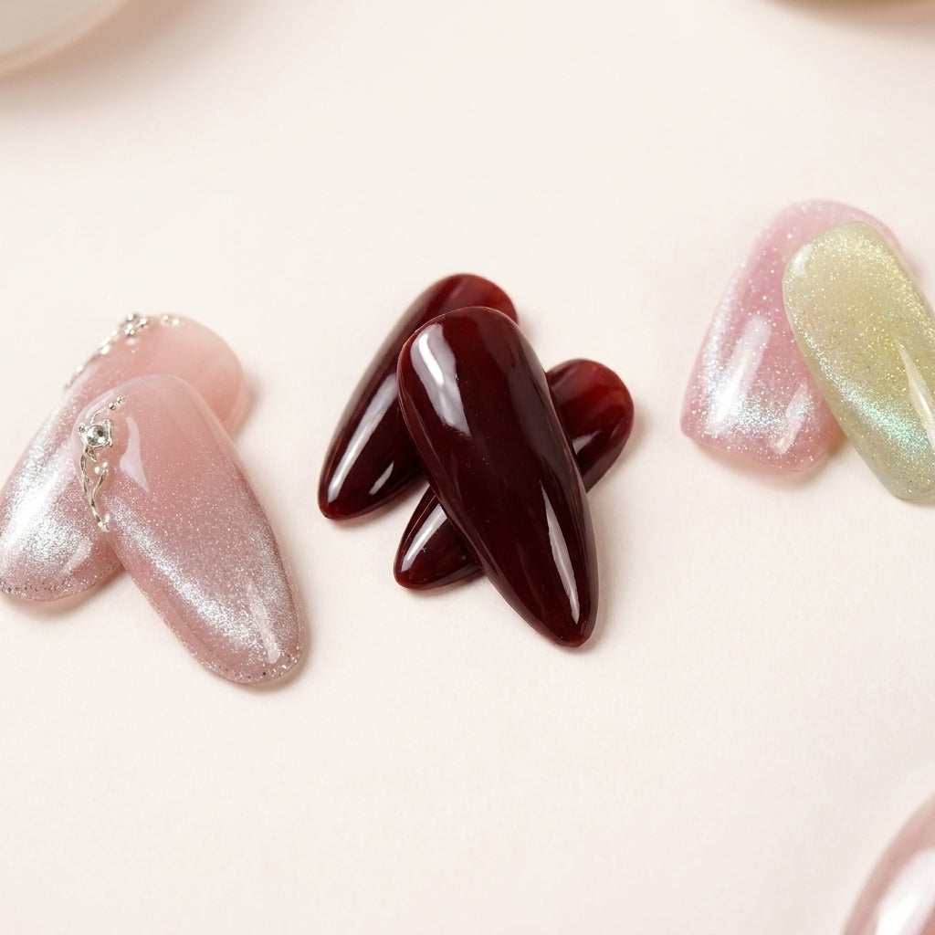 Makro-nærbilde av The Minimalist Edit-nagler — Angel Glaze med sølv glitter-ombré og kjede-detalj, Cherry on Top i dyp glossy burgunder og Cotton Candy i pastell chrome.