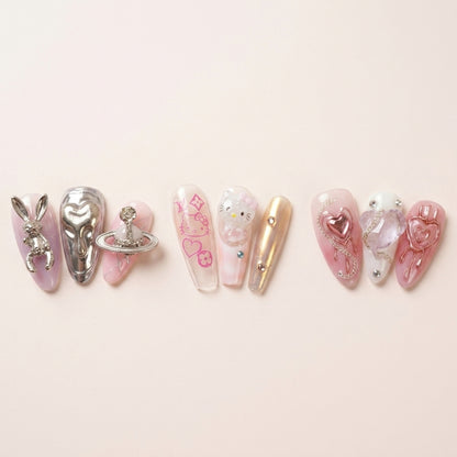Nærbilde-triptyk av The Y2K Edit-nagler — Astro Bunny med sølv kanin og Saturn-charm, Y2K Royalty med Hello Kitty og logo-print, Pretty in Pain med rosa chrome-hjerter.